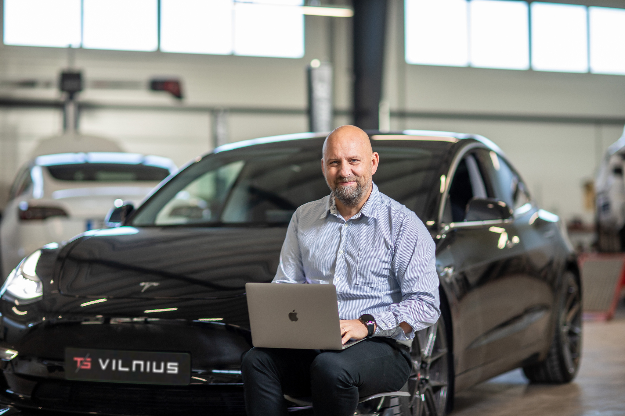 „TS Vilnius“ atstovas su nešiojamuoju kompiuteriu prie Tesla automobilio dirbtuvėse