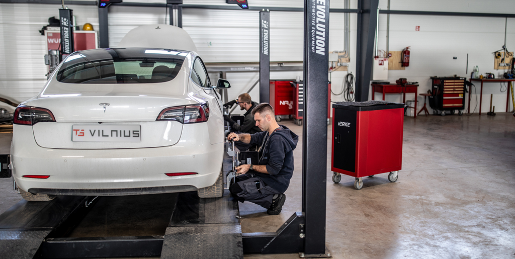 Meistras dirba prie balto Tesla automobilio „TS Vilnius“ remonto dirbtuvėse