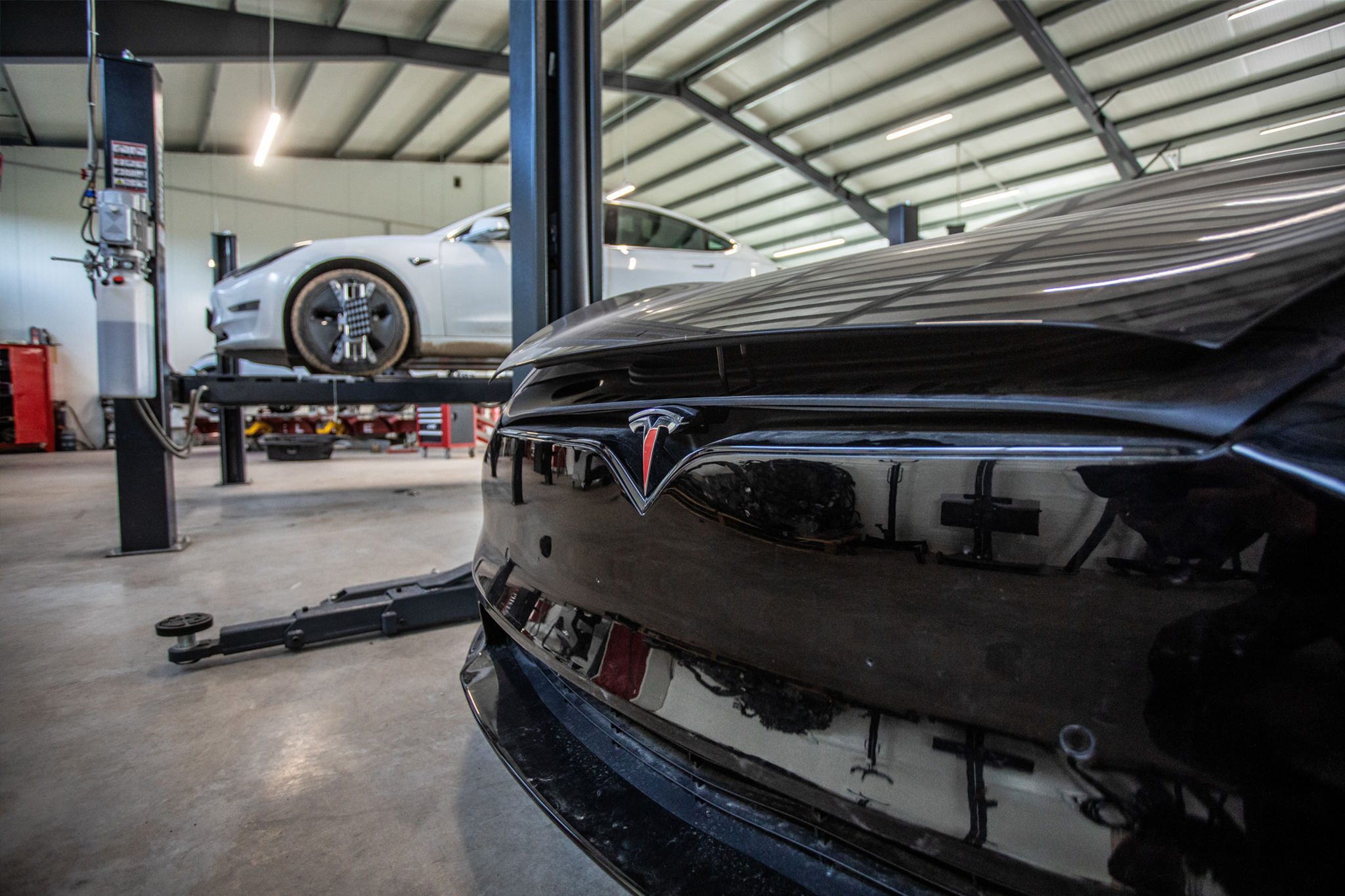 Tesla automobilio priekinė dalis ir kitas automobilis ant keltuvo „TS Vilnius“ dirbtuvėse